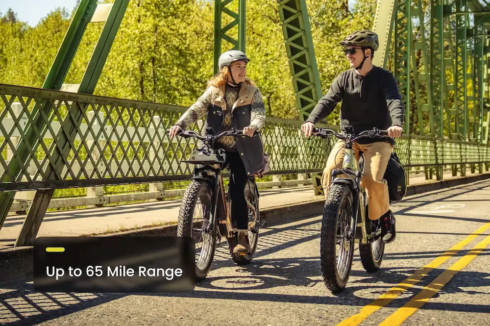 Two people riding electric bikes on a bridge with greenery in the background